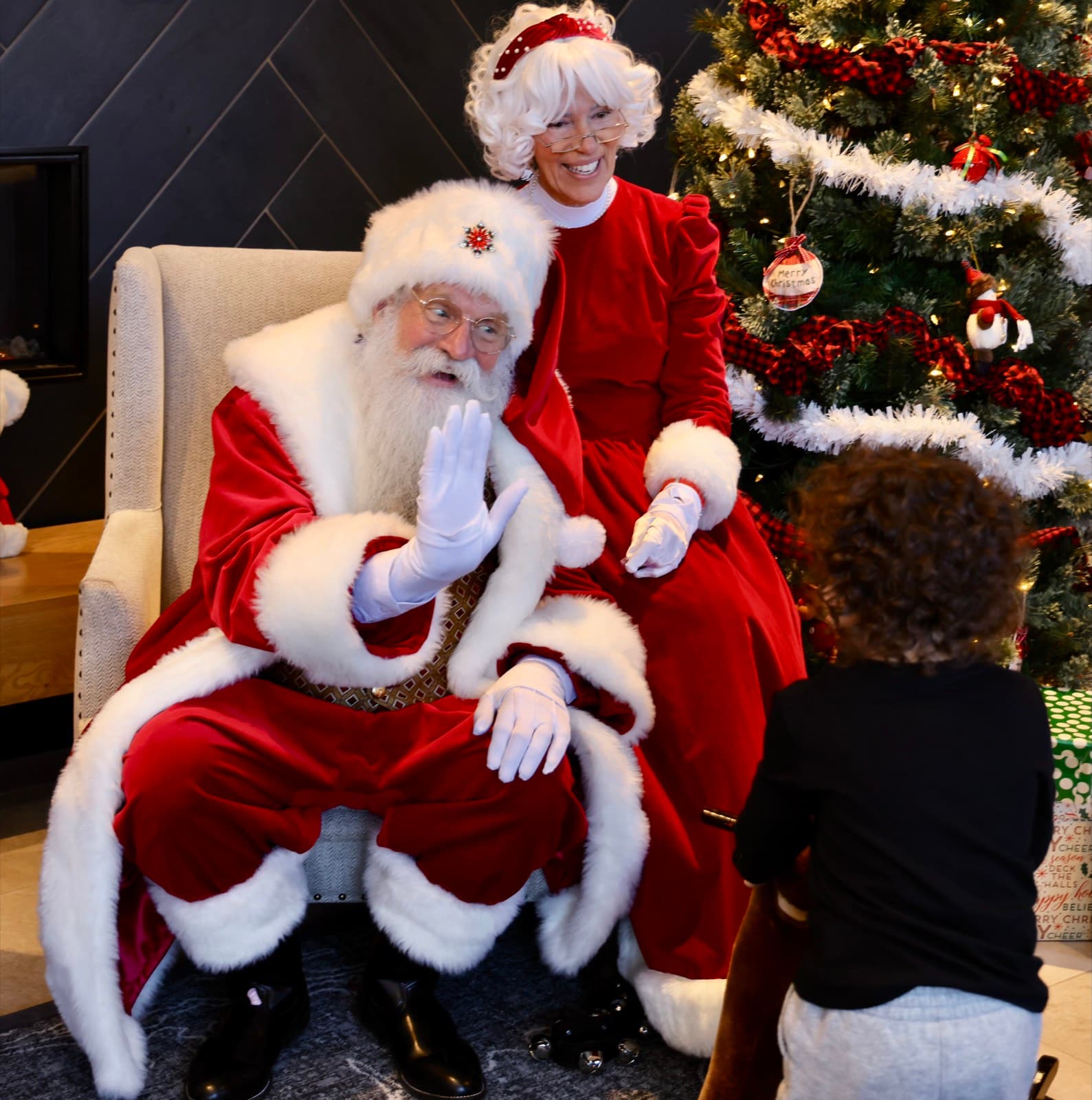 Santa and Mrs. Claus greeting a child by the Christmas tree